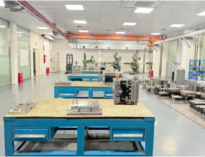 Workbenches with metal tooling and an overhead crane in a workshop.